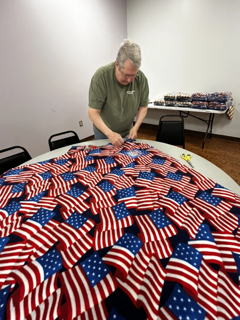 Volunteer tying fringe on an American flag print no-sew blanket at the BV Mall Senior Center