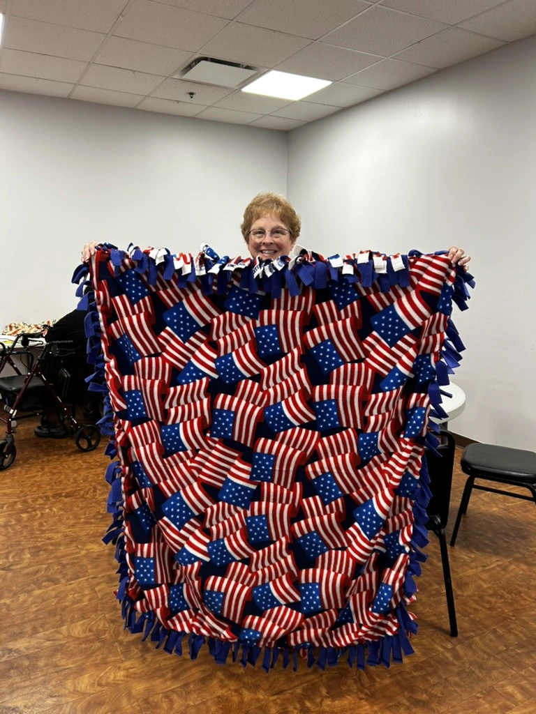 Volunteer holding a finished no-sew fleece blanket with American flag pattern at the BV Mall Senior Center