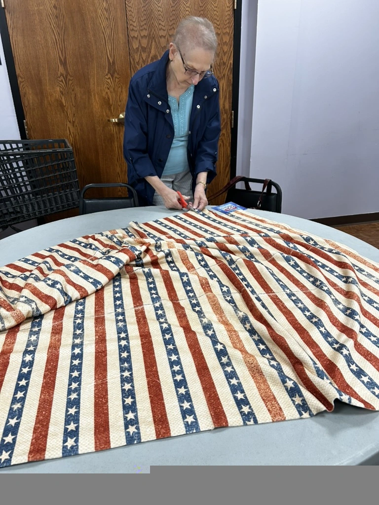 Volunteer cutting fringe on a patriotic stars and stripes no-sew blanket at the BV Mall Senior Center